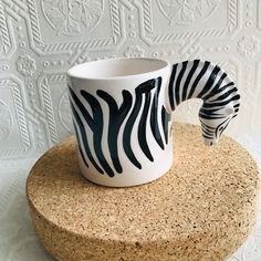 a ceramic zebra coffee cup sitting on top of a cork coaster next to a white wall