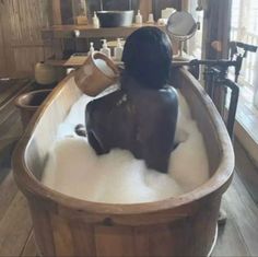 a bath tub filled with lots of foam and water next to a wooden floored wall