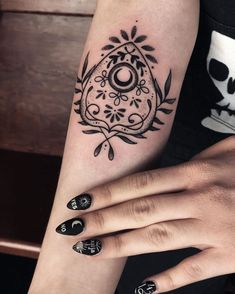 a woman's arm with black and white tattoos on her left hand, holding a skull