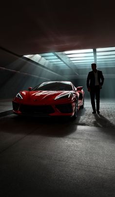 a man standing next to a red sports car in a dark garage with the door open