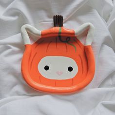 an orange and white plate with a cat on it's face, sitting on a bed