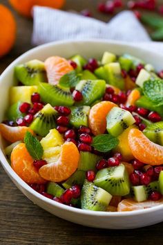 a white bowl filled with fruit salad on top of a wooden table next to oranges