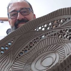 a man holding up a large piece of art made out of clay with holes in it