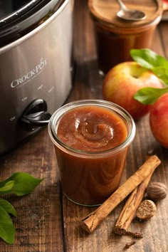 an apple cider, cinnamon sticks and apples sit next to the crock pot