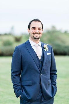 a man in a blue suit and white shirt smiles at the camera with his hands in his pockets