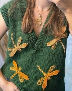 a woman wearing a green sweater with yellow dragonflys on it and holding a cell phone up to her ear