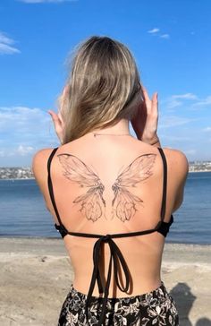 a woman with a butterfly tattoo on her back is looking out at the water and beach