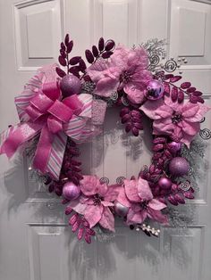 a wreath with pink flowers and purple balls hanging on the front door to welcome guests