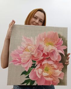 a woman holding up a painting with pink flowers on it