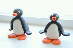 two plastic penguins sitting next to each other on a window sill, one with an orange beak