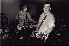 black and white photograph of two men playing guitars in a room full of other people