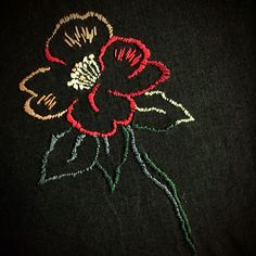 a black t - shirt with red and green flowers on the front, embroidered onto it