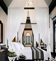 a white bed with black and white bedspread in a bedroom next to windows