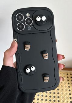 a person holding up a cell phone case with buttons and eyes on it in front of a white wall