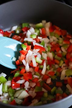 chopped vegetables being cooked in a pan with a blue spoon