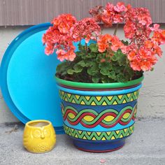 a potted plant sitting next to a blue plate and yellow vase with flowers in it