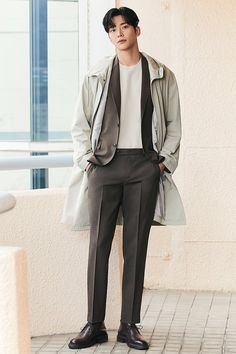 a young man standing in front of a building wearing a gray suit and black shoes