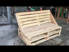 a wooden bench made out of pallets sitting on top of cement floor next to a building