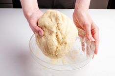 a person is kneading dough into a glass bowl on a white countertop