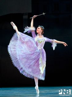 the ballerina is dressed in purple and has her arms stretched out with one hand