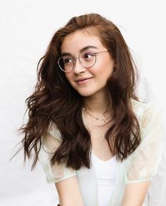 a young woman with glasses is posing for a photo in front of a white background