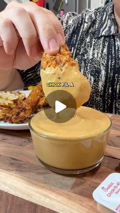 a person dipping something into a bowl on top of a wooden table next to food