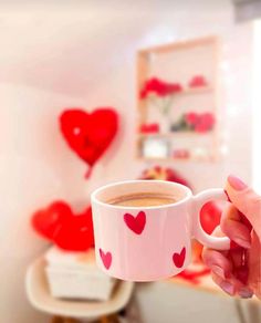 a person holding a cup of coffee with hearts on the wall in the back ground