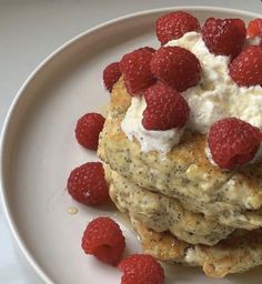 a white plate topped with pancakes covered in cream and raspberries