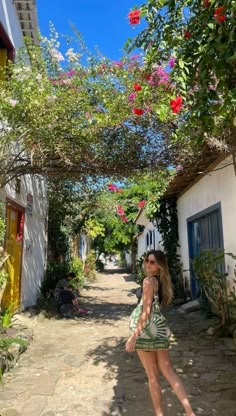 a woman standing in the middle of an alley way with flowers growing over her head