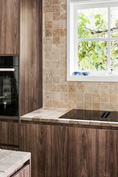 a kitchen with marble counter tops and wooden cabinets, along with a window that looks out onto the trees outside