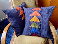 two decorative pillows on a chair with a blue rug in the corner and a wooden arm chair