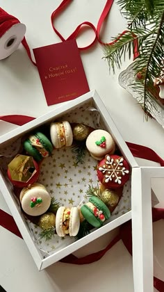 an open box filled with christmas cookies next to a red and white ribbon on a table