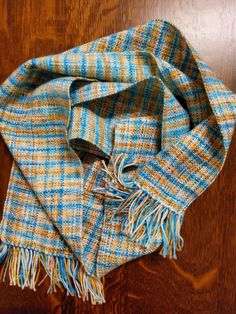 a blue and yellow plaid scarf laying on top of a wooden floor next to a brown table