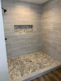 a walk in shower sitting next to a wooden floor covered in gray tile and stone