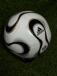 a white soccer ball with black and gold stripes on the side sitting in grass, top view