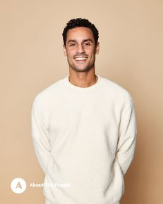 a man in a white sweater smiling for the camera with his hands in his pockets