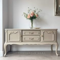 a vase with flowers sitting on top of a white dresser next to a framed mirror