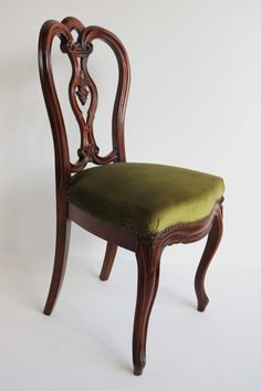 an antique wooden chair with green velvet upholstered seat and back cushion on white background