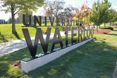 the university of waterloo sign is in front of some trees and grass on a sunny day