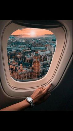 a person's hand on the window of an airplane looking out at london and big ben