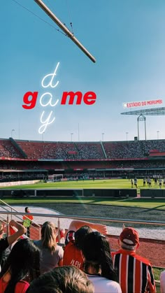 people are sitting in the stands at a baseball game and there is a neon sign that says it's game y