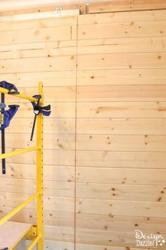 a yellow scaffold in front of a wooden wall with tools hanging on it