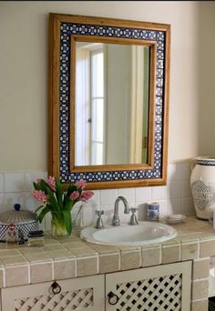 a bathroom sink with a mirror above it and flowers in the vase on the counter