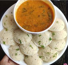 a white plate topped with dumplings next to a bowl of soup and dipping sauce