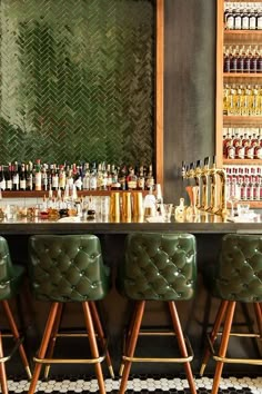 a bar with green chairs and bottles on the wall behind it, along with shelves full of liquor