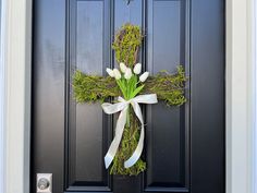 a cross made out of moss and flowers hangs on the front door of a house