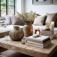 a coffee table with books, candles and vase on it in front of a couch