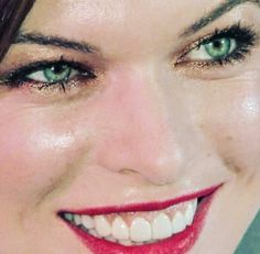 a close up of a woman with green eyes and red lipstick smiling at the camera