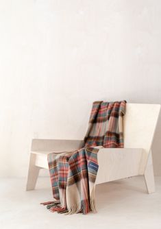 a plaid blanket sitting on top of a wooden bench next to a white wall and floor