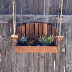 a wooden swing with succulents and plants in it hanging on a fence